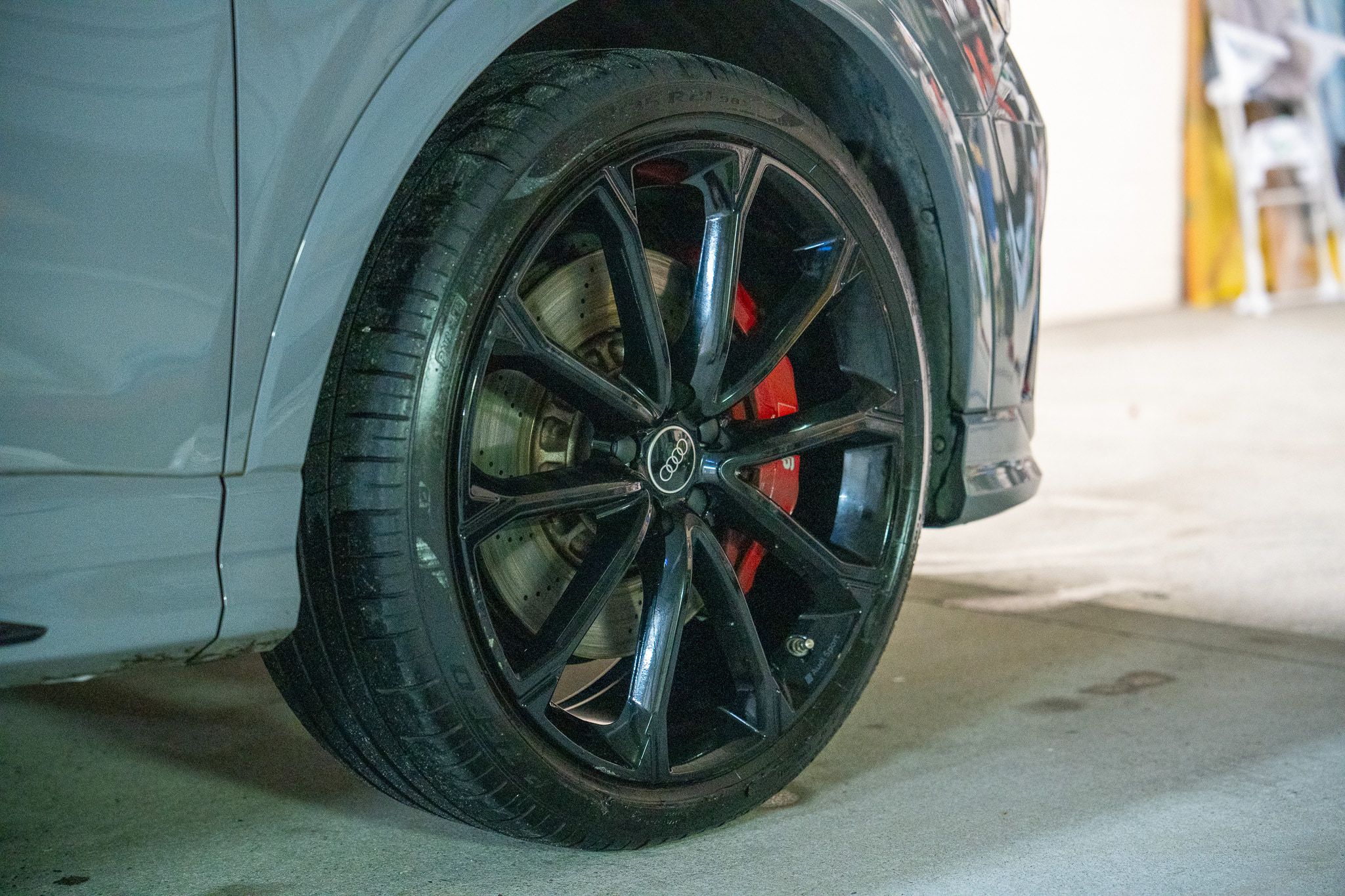 Gloss-black Audi RS Q3 wheel and red brake caliper beside clean Nardo grey paint